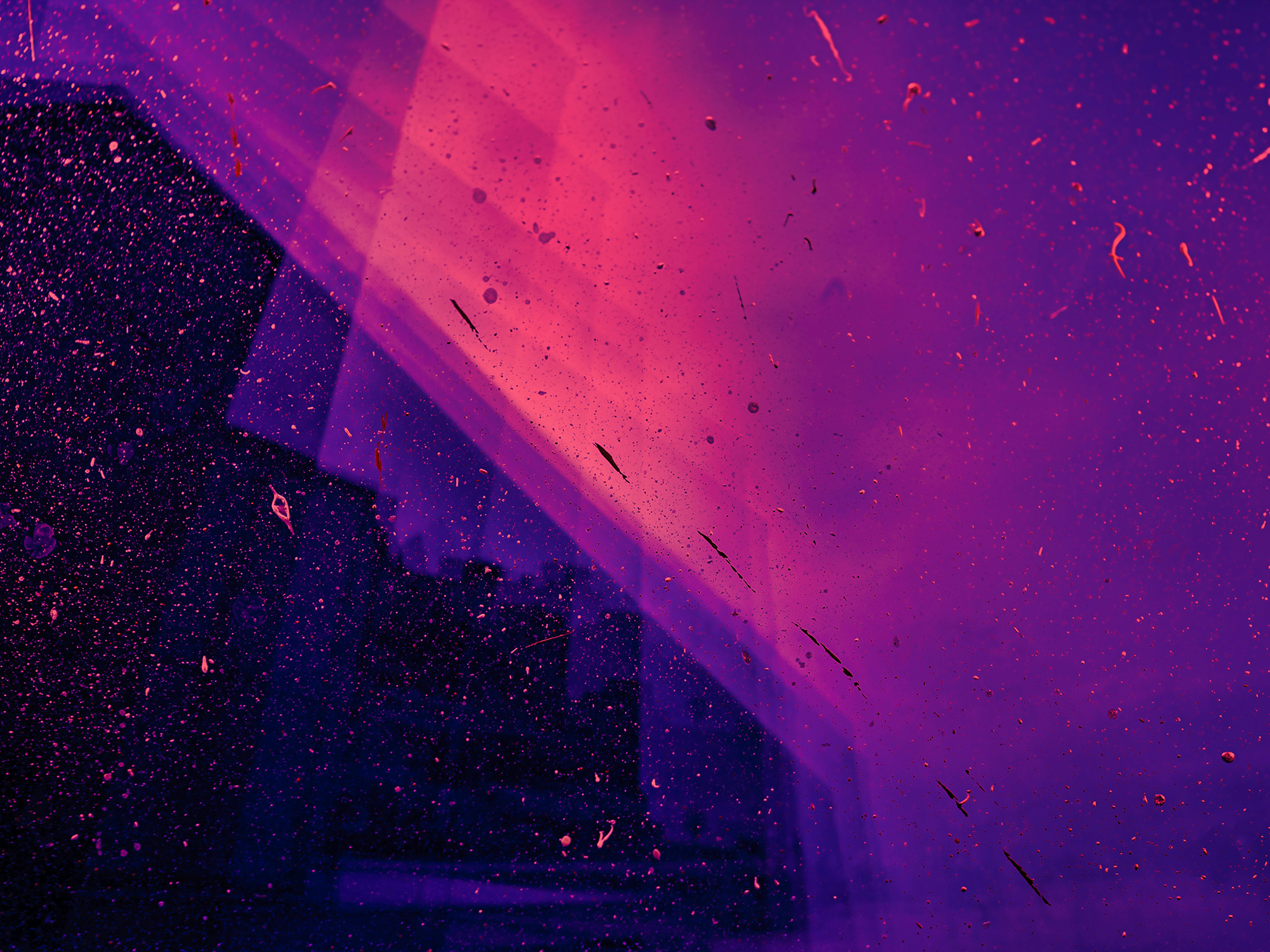 Streaks of pink and purple light falling across a dark, dust-speckled pane of glass